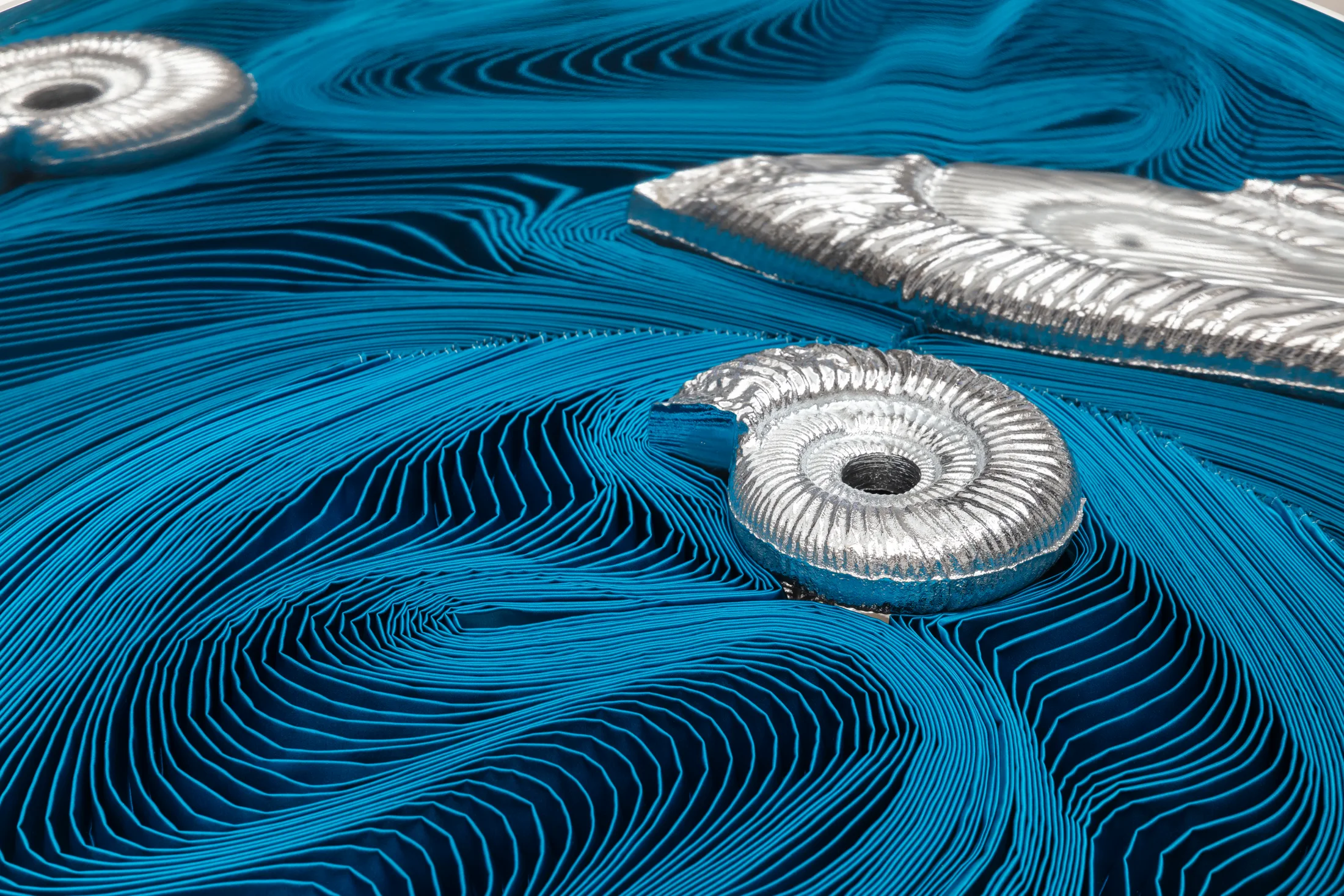 A detail of a sculpture by Alice Channer of pleated satin silk with cast silver ammonites sat on top