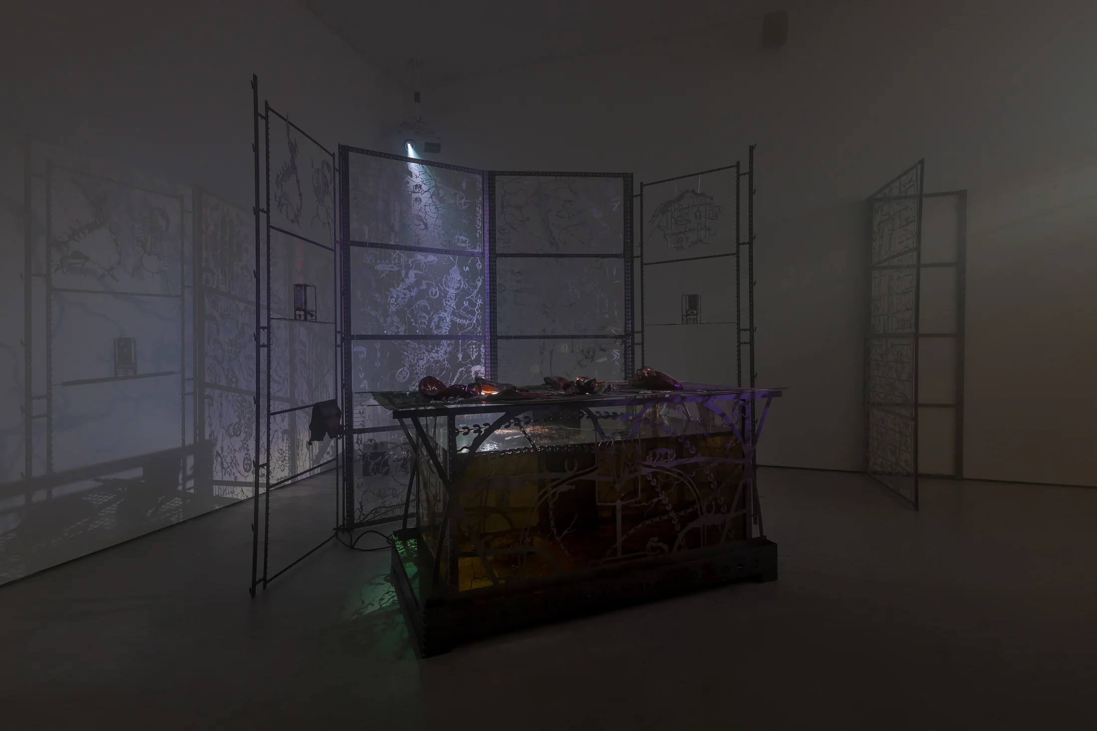 An installation by Hazel Brill including a water tanks filled with a dark liquid laser cut steel dividers, mouth-blown glass objects, projections and lights