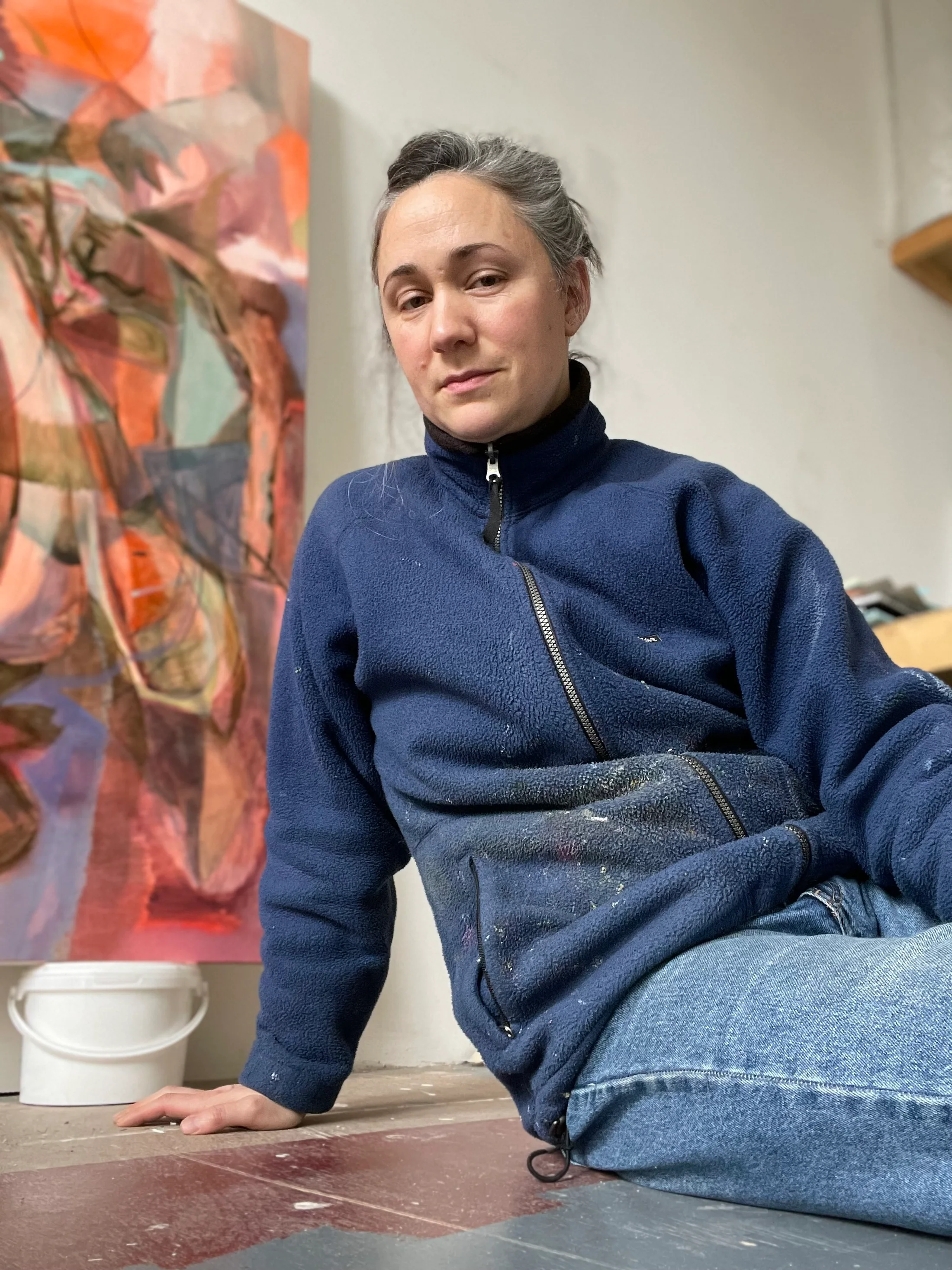 Portrait of artist Amy Winstanley sitting in her studio in front of a painting